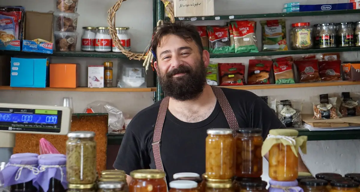Een winkelier achter de toonbank van zijn zaak met potten en producten